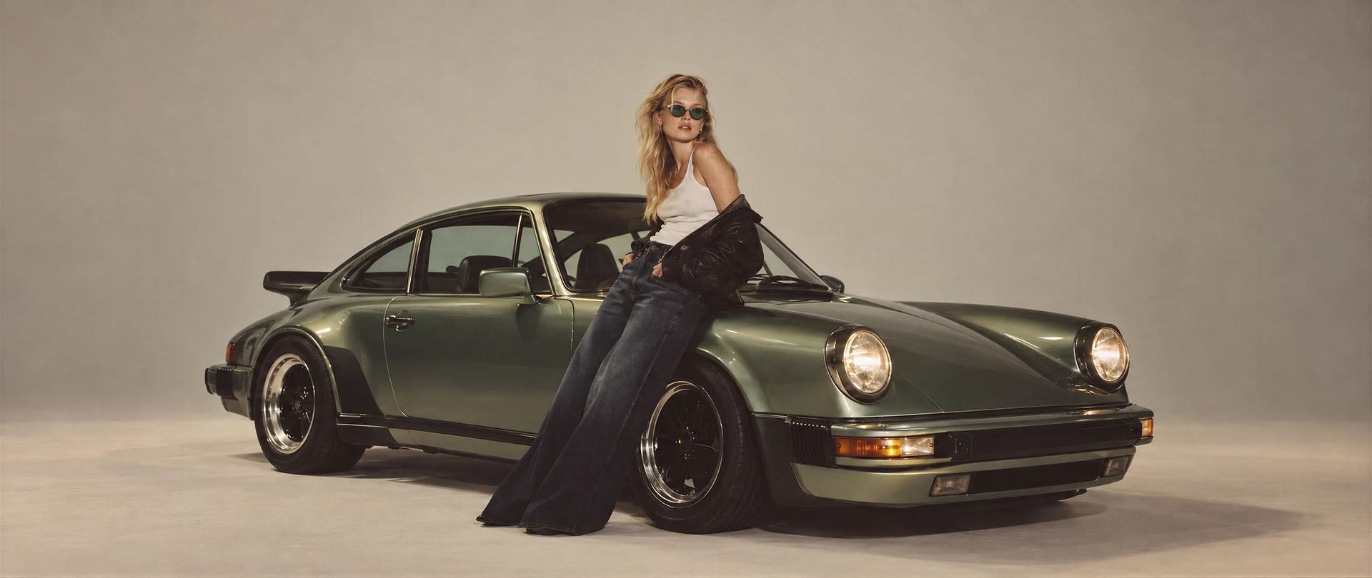 Mujer con anteojos de sol en una escena editorial junto a un auto clásico